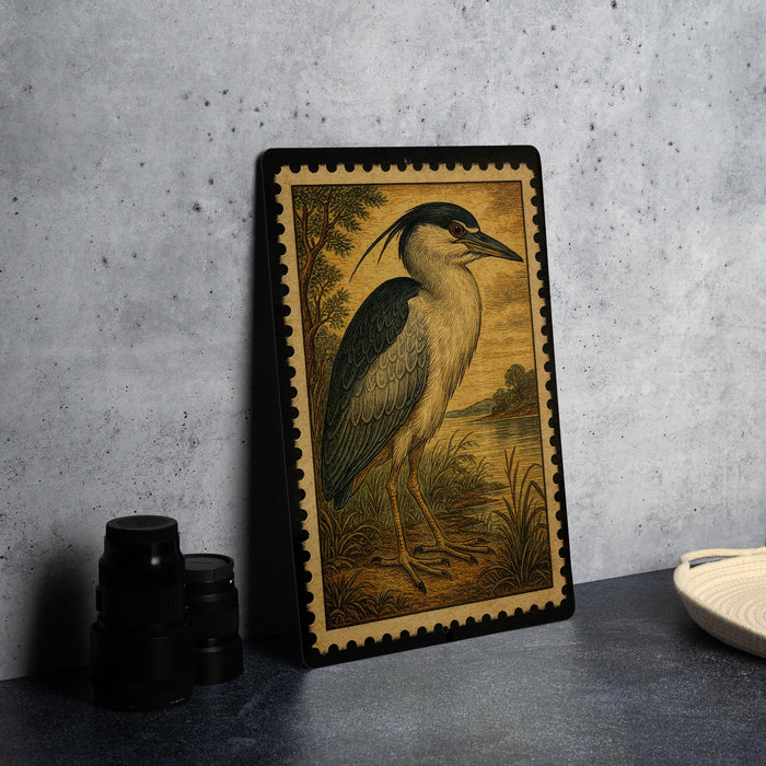 a framed illustration of a bird, likely a heron, standing on a grassy area with a body of water in the background.