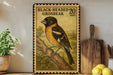 A framed postage stamp depicting a black-headed grosbeak, with a wooden cutting board and lemons in the foreground.