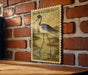 a vintage-style stamp or postcard with a black-necked stilt illustration on a brick wall.
