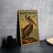 A framed illustration of a pelican is displayed on a wall, with a small white bowl and a stack of black camera lenses to the left.