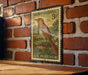 A vintage brown thrasher postage stamp is displayed on a brick wall, featuring a detailed illustration of a bird perched on a branch.