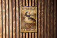A vintage-style postage stamp featuring a duck is displayed on a wooden wall.