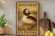 A vintage-style metal stamp depicting a duck, with the text "BUFFLEHEAD U.S. POSTAGE" printed on it. The stamp is placed on a shelf next to a wooden cutting board and a potted plant.