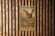 A U.S. postage stamp featuring a bird perched on a branch, mounted on a wooden wall.