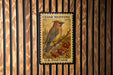 A U.S. postage stamp featuring a bird perched on a branch with berries, mounted on a wooden wall.