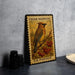 A vintage-style postage stamp featuring a bird perched on a branch with berries, placed on a countertop next to some black camera lenses.