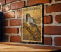 a vintage-style postage stamp with a detailed illustration of a bird perched on a branch, set against a brick wall.