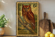 A framed stamp depicting an Eastern Screech Owl, with the text "EASTERN SCREECH OWL" printed on it. The stamp is placed on a shelf next to a wooden cutting board and a potted plant.