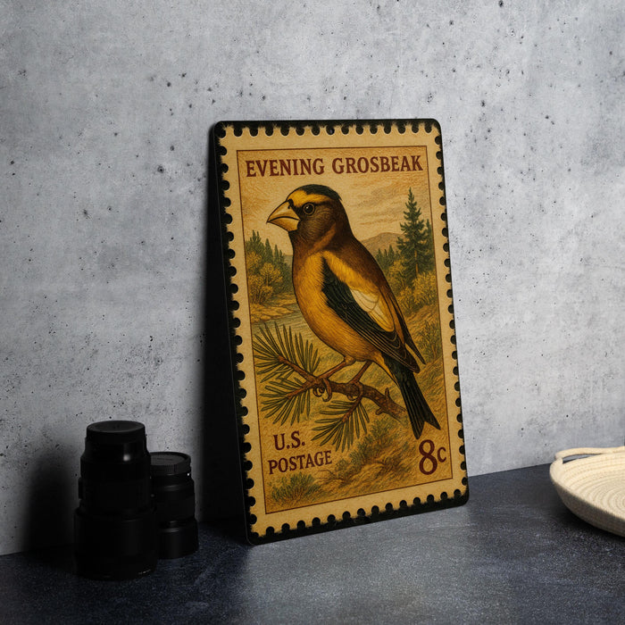 A U.S. postage stamp featuring a golden bird perched on a branch, with the text "Evening Grosbeak" and "U.S. Postage" printed on it.