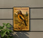 a postage stamp with a bird illustration, mounted on a wall next to a plant.