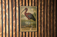 A postage stamp featuring a red and brown bird, likely a stork, is displayed on a wooden wall.