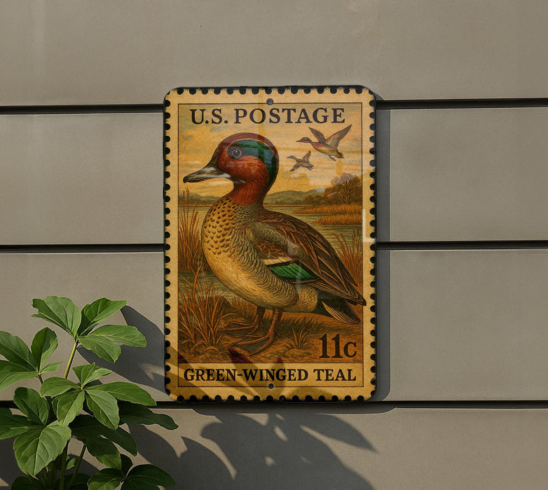 A U.S. postage stamp featuring a green-winged teal duck, mounted on a wall next to a plant.