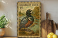 A vintage postage stamp featuring a harlequin duck, with a wooden cutting board and lemons in the foreground.
