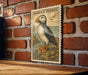 A framed illustration of a puffin bird is displayed on a brick wall.