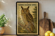 a framed illustration of a long-eared owl perched on a branch, with a potted plant to the left and a wooden cutting board to the right.