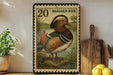 A framed postage stamp depicting a colorful mandarin duck is displayed on a shelf next to a wooden cutting board and some lemons.