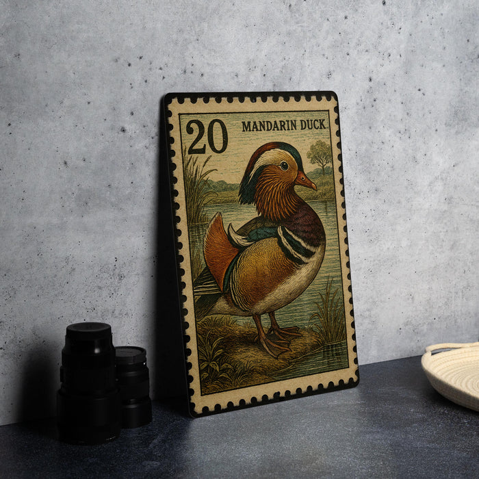 A framed postage stamp featuring a colorful illustration of a mandarin duck, placed on a table next to some black camera lenses.