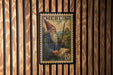 A vintage-style postage stamp featuring a bearded man in a conical hat, holding a book and standing in front of a castle.