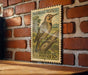 A vintage postage stamp featuring a brown and black spotted bird, likely a Northern Flicker, is displayed on a brick wall.