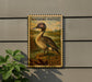 A postage stamp featuring a duck is displayed on a wall, with a plant visible to the left.