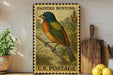 A framed painting of a colorful bird, likely a painted bunt, is displayed on a shelf next to a wooden cutting board and some lemons.