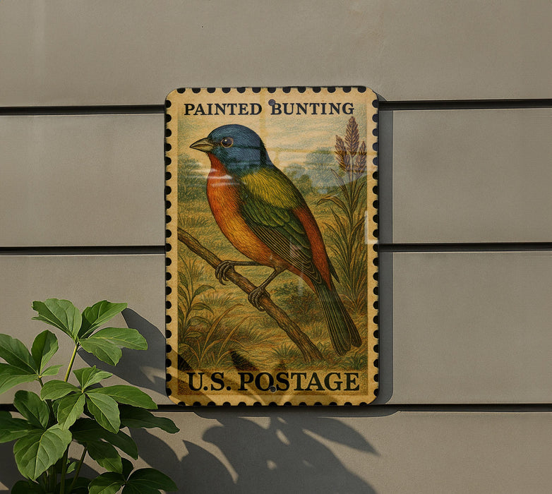 A painted bunt bird postage stamp is displayed on a wall, with a plant to the left.