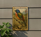 A painted bunt bird postage stamp is displayed on a wall, with a plant to the left.