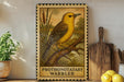 a framed illustration of a yellow warbler perched on a branch, with a wooden cutting board and a potted plant in the background.