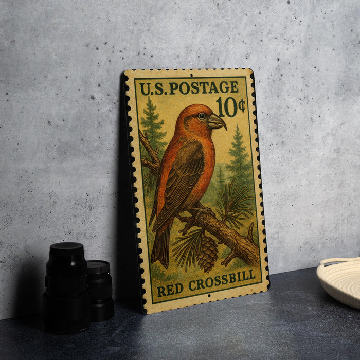A U.S. postage stamp featuring a red crossbill bird, placed on a gray surface next to some black camera lenses.