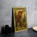 A U.S. postage stamp featuring a red crossbill bird, placed on a gray surface next to some black camera lenses.