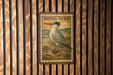 A metal sign with a bird illustration is mounted on a wooden wall.