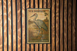 A U.S. postage stamp featuring a sandhill crane, which is a type of crane, is displayed on a wooden wall.