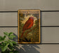 a red bird perched on a branch, with a plant to the left of the frame.