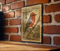a vintage-style metal stamp with a detailed illustration of a red-headed bird perched on a branch, mounted on a brick wall.