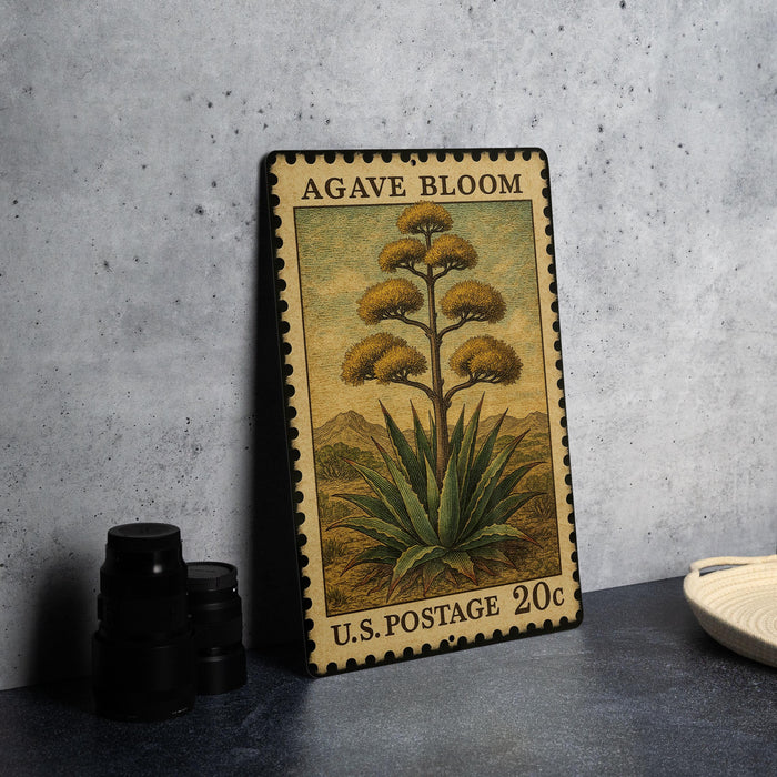 A metal sign with a postage stamp design, featuring an illustration of an agave plant, is displayed on a table.