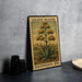 A metal sign with a postage stamp design, featuring an illustration of an agave plant, is displayed on a table.