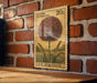 A vintage 20c U.S. postage stamp featuring a large flower illustration is displayed on a brick wall.
