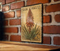 A vintage-style aloe vera postage stamp is displayed on a brick wall, featuring a detailed illustration of the aloe vera plant.