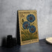 A U.S. postage stamp featuring a blue flower design, placed on a table next to some black camera lenses.