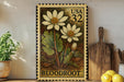 A framed image of a white flower with yellow centers, labeled "Bloodroot", is displayed on a shelf next to a wooden cutting board and a potted plant.