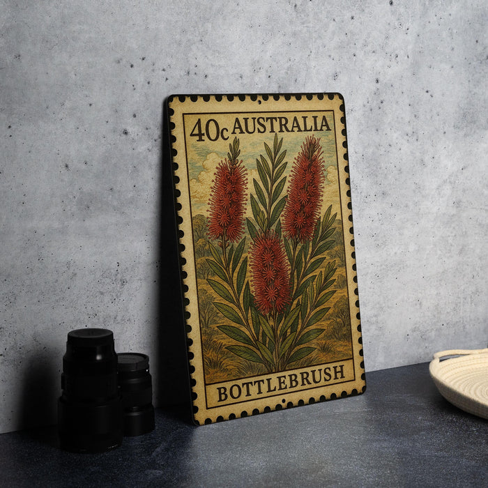 A metal sign with a floral design and text, placed on a countertop next to some black camera lenses.