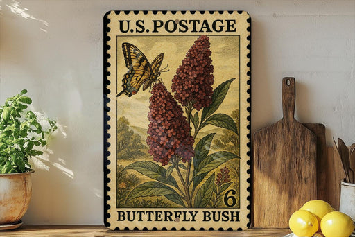 A vintage U.S. postage stamp featuring a butterfly and a flowering bush, with the text "Butterfly Bush" printed on it. The stamp is displayed on a shelf next to a wooden cutting board and a potted plant.