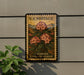 A U.S. postage stamp featuring a floral design, mounted on a wall next to a plant.