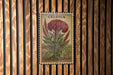 a large, detailed illustration of a red flower with green leaves, mounted on a wooden wall.