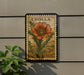 A vintage postage stamp featuring a large orange flower is displayed on a wall, with a plant to the left.