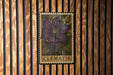 A framed image of a purple clematis flower is displayed on a wooden wall.