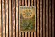 A vintage-style stamp featuring a flower with the word "COWSLIP" printed on it, displayed on a wooden wall.
