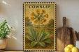 a framed illustration of a yellow flower with green leaves, placed on a shelf next to a wooden cutting board and a potted plant.