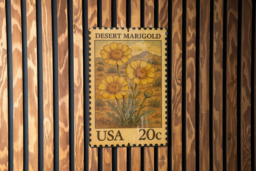 A United States postage stamp featuring a desert marigold flower is displayed on a wooden wall.
