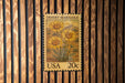 A United States postage stamp featuring a desert marigold flower is displayed on a wooden wall.